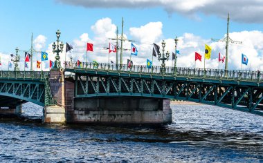 Köprünün kemerlerini indiriyorum, bayramın onuruna renkli bayraklarla süslenmiş mavi gökyüzü ve bulutların arka planına karşı