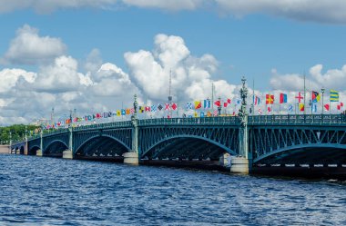 St. Petersburg, Rusya 'daki Neva nehri üzerindeki metal açılış köprüsü, mavi gökyüzü ve bulutların arka planına karşı bayramın onuruna bayraklarla süslenmiştir..