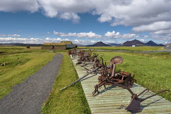 Pathway to farm houses in Modrudalur settlement of Eastern Island, old agricultural equipment for soil cultivation is installed  in wooden path along the walk path, Modrudalsjallgardar mountain landscape is at background