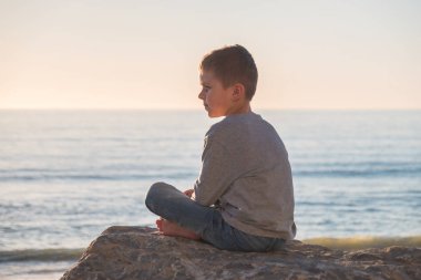 Glenelg kumsalda kayaya oturan ve hayat hakkında düşünme yalnız yalınayak çocuk
