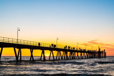 Stunning sunset at Glenelg Beach jetty, with silhouettes of people leisurely strolling along the pier in Adelaide, South Australia