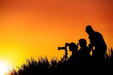 Fotoğrafçılar grup günbatımı evenin içinde çim tepede silüeti