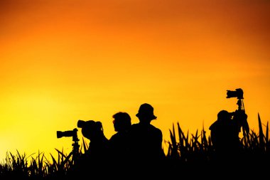 Fotoğrafçılar grup günbatımı evenin içinde çim tepede silüeti