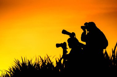 Fotoğrafçılar grup günbatımı evenin içinde çim tepede silüeti