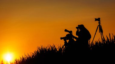 Fotoğrafçılar grup günbatımı evenin içinde çim tepede silüeti
