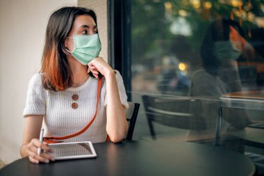 Asyalı iş kadını cerrahi maske takıyor. Karantina Coronavirus covid-19 salgını sırasında tablet kullanıyor..