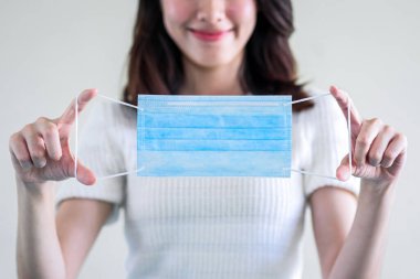 Genç ve güzel Asyalı bir kadın tıbbi maske takmayı ya da beyaz arka planda adım adım hijyen maskesi takmayı öğretiyor.