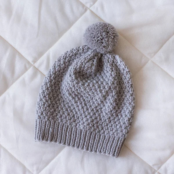 Grey knitted hat with a small pompom on a white blanket