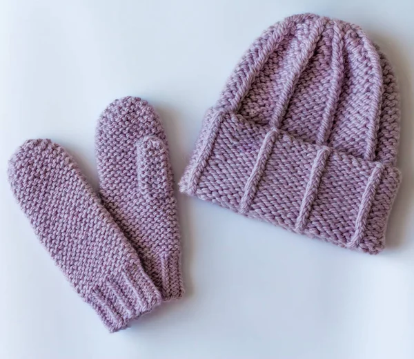 Hat and mittens connected by hand from wool on wooden background