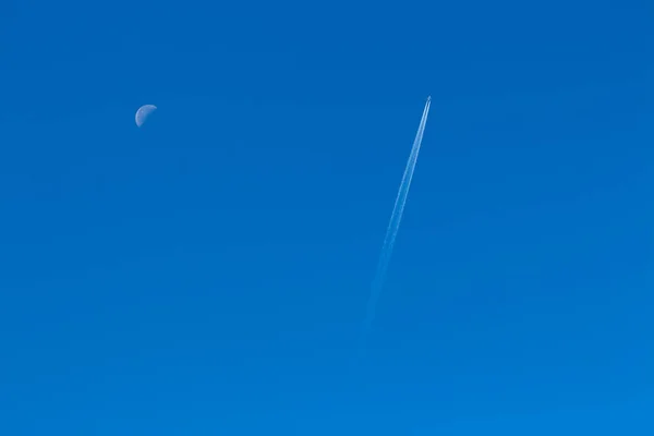 Plane in a clear sky, reversing the track from him and half moon — Stock Photo, Image