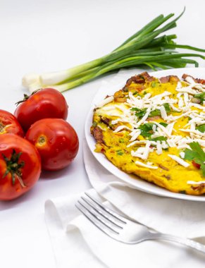Taze yeşil soğan ve domatesle servis edilen lezzetli omlet ve beyaz dekorun üstünde rendelenmiş peynir.