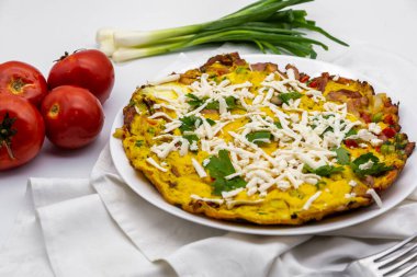 Taze yeşil soğan ve domatesle servis edilen lezzetli omlet ve beyaz dekorun üstünde rendelenmiş peynir.