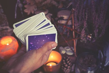 Kadın eli tarot destesi ya da falcılık yapan kahin kartları tutuyor. Gölgelerde soğuk renklere bürünmüş.