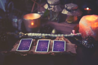 3 Tarot kartı sihirli eşyalarla birlikte siyah bir masaya yayılmış. Gölgelerde soğuk renklere bürünmüş.