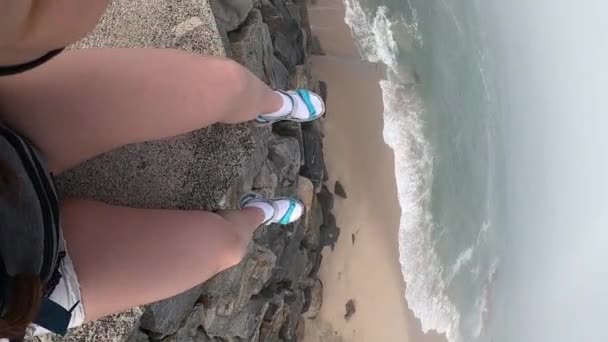Жіночі ніжки з видом на Атлантичний океан. Порожній пляж в Povoa де Варзім, Португалія на Туманний осінній день з хвилями гуркіт на березі нижче і туман в далечині. Вертикальний відеокадр 9:16. — стокове відео