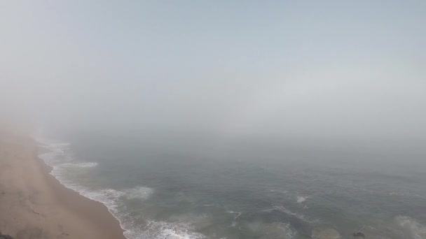 Mujer mirando el horizonte con el océano en Portugal. Playa vacía en Povoa de Varzim, Portugal en el día de otoño brumoso con olas que se estrellan en la orilla y niebla en la distancia . — Vídeos de Stock