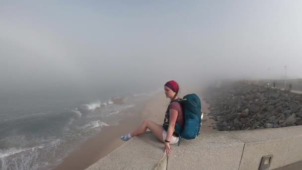 Kobieta patrząc na horyzoncie z oceanu w Portugalii. Pusta plaża w Povoa de Varzim, Portugalia na mgliste jesienny dzień z falami upaść na brzegu poniżej i mgła w odległości. — Wideo stockowe