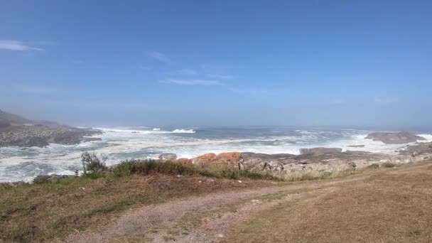 View of the Atlantic Ocean. On the way to Oia, Spain on a sunny day with waves. Water beats against stones on the shore. Way of Santiago. Pilgrims Road. — Stock Video