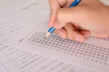 Öğrenciler, cevap kağıtları ve matematik soru kağıtları üzerinde seçilmiş kalemle yazı yazma seçeneğini el ele tutuyorlar. Sınav yapan öğrenciler. okul sınavı 