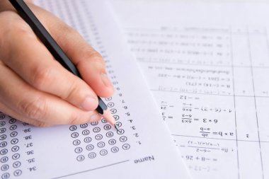 Öğrenciler, cevap kağıtları ve matematik soru kağıtları üzerinde seçilmiş kalemle yazı yazma seçeneğini el ele tutuyorlar. Sınav yapan öğrenciler. okul sınavı 
