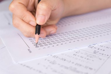 Öğrenciler, cevap kağıtları ve matematik soru kağıtları üzerinde seçilmiş kalemle yazı yazma seçeneğini el ele tutuyorlar. Sınav yapan öğrenciler. okul sınavı 