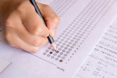 Öğrenciler, cevap kağıtları ve matematik soru kağıtları üzerinde seçilmiş kalemle yazı yazma seçeneğini el ele tutuyorlar. Sınav yapan öğrenciler. okul sınavı 