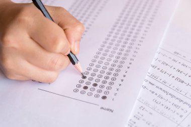 Öğrenciler, cevap kağıtları ve matematik soru kağıtları üzerinde seçilmiş kalemle yazı yazma seçeneğini el ele tutuyorlar. Sınav yapan öğrenciler. okul sınavı 