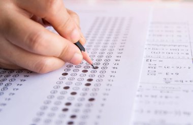 Öğrenciler, cevap kağıtları ve matematik soru kağıtları üzerinde seçilmiş kalemle yazı yazma seçeneğini el ele tutuyorlar. Sınav yapan öğrenciler. okul sınavı 