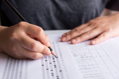 Öğrenciler, cevap kağıtları ve matematik soru kağıtları üzerinde seçilmiş kalemle yazı yazma seçeneğini el ele tutuyorlar. Sınav yapan öğrenciler. okul sınavı 