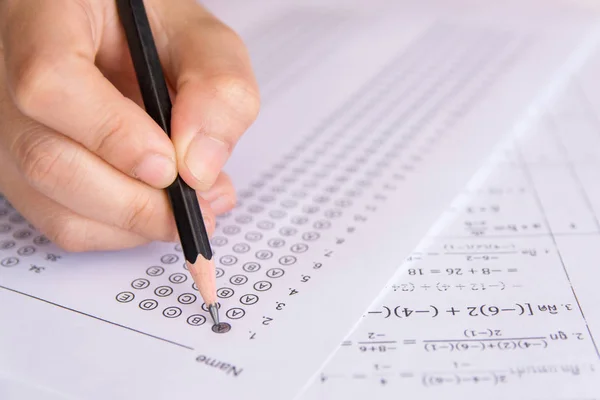 Students hand holding pencil writing selected choice on answer sheets and Mathematics question sheets. students testing doing examination. school exam