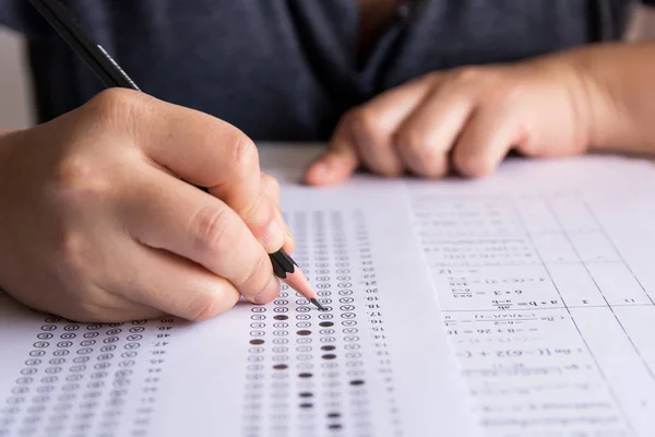 Öğrenciler, cevap kağıtları ve matematik soru kağıtları üzerinde seçilmiş kalemle yazı yazma seçeneğini el ele tutuyorlar. Sınav yapan öğrenciler. okul sınavı 