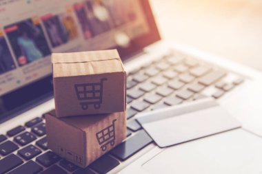 Online kavramı alışveriş - online web üzerinde hizmet alışveriş. ödeme kredi kartı ve teklifler eve teslim. bir dizüstü bilgisayar klavye logosuna parsel veya kağıt karton bir alışveriş sepeti