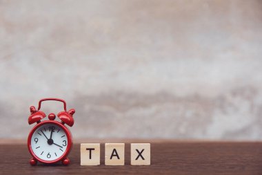 Tahta alfabe blokları olan vergiler, kırmızı alarm saati, koyu tahta üzerinde. 