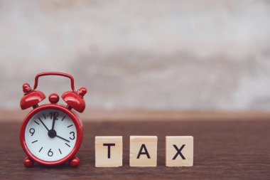 Tahta alfabe blokları olan vergiler, masa karanlığında kırmızı alarm saati. 