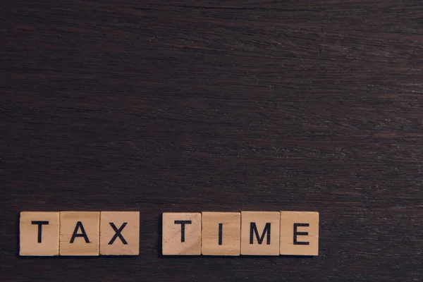 Время уплаты налогов с деревянными алфавитными блоками на темной доске деревянного бэкгра — стоковое фото