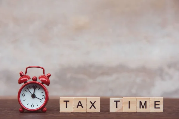 Время уплаты налогов с алфавитным деревянным кубом и красным будильником — стоковое фото