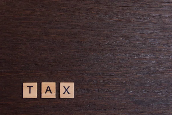 Steuer mit Buchstabenblöcken aus Holz, auf dunklem Holzuntergrund — Stockfoto