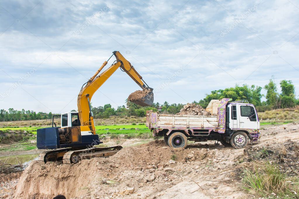 Yellow excavator machine loading soil into a dump truck at const