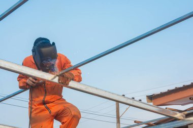 Çatı kirişleri için turuncu iş elbiseleri kaynak yapan bir işçi.