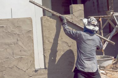 İnşaat işçileri inşaat duvarlarını beton kaplamalarıyla sıva yapıyorlar.