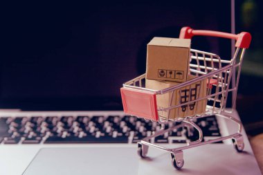 İnternetten alışveriş konsepti - Paket ya da kağıt kutular içinde alışveriş arabası logosu ve dizüstü bilgisayarda klavye. İnternet 'te alışveriş servisi. Eve teslimat teklif ediyor