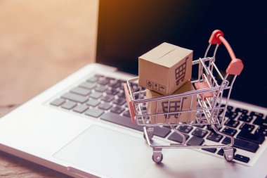 İnternetten alışveriş konsepti - Paket ya da kağıt kutular içinde alışveriş arabası logosu ve dizüstü bilgisayarda klavye. İnternet 'te alışveriş servisi. Eve teslimat teklif ediyor
