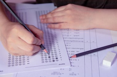 Öğrenciler, cevap kağıtları ve matematik soru kağıtları üzerinde seçilmiş kalemle yazı yazma seçeneğini el ele tutuyorlar. Sınav yapan öğrenciler. Okul çıkışı.