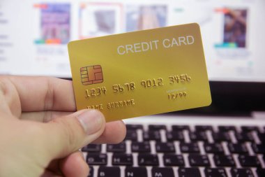 Kredi kartı tutan ve dizüstü bilgisayar kullanan bir kadın çevrimiçi ödeme yapıyor.