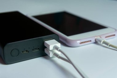 Beyaz masadaki elektrik bankasıyla çalışan akıllı telefon.