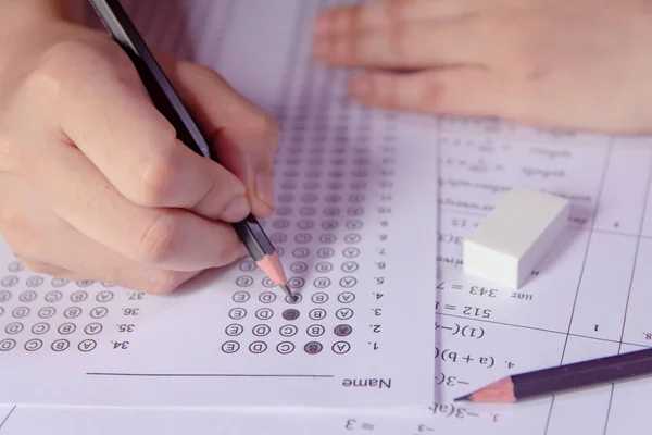 Students hand holding pencil writing selected choice on answer sheets and Mathematics question sheets. students testing doing examination. school exa