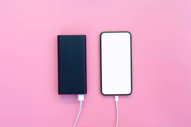 Pembe arka planda elektrik bankasıyla şarj olan akıllı telefon. Kopyalama alanı için kırpma yolu olan beyaz ekran veya boş ekran. Düz yatıyordu
