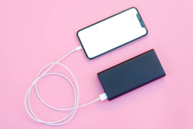 Pembe arka planda elektrik bankasıyla şarj olan akıllı telefon. Kopyalama alanı için kırpma yolu olan beyaz ekran veya boş ekran. Düz yatıyordu