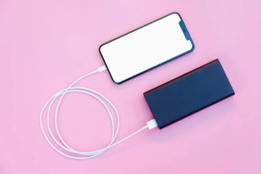 Pembe arka planda elektrik bankasıyla şarj olan akıllı telefon. Kopyalama alanı için kırpma yolu olan beyaz ekran veya boş ekran. Düz yatıyordu