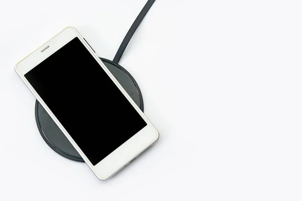 白い背景にワイヤレス充電器でスマートフォンの充電 コピースペースのクリッピングパスを持つ黒い画面または空白の画面 フラット — ストック写真